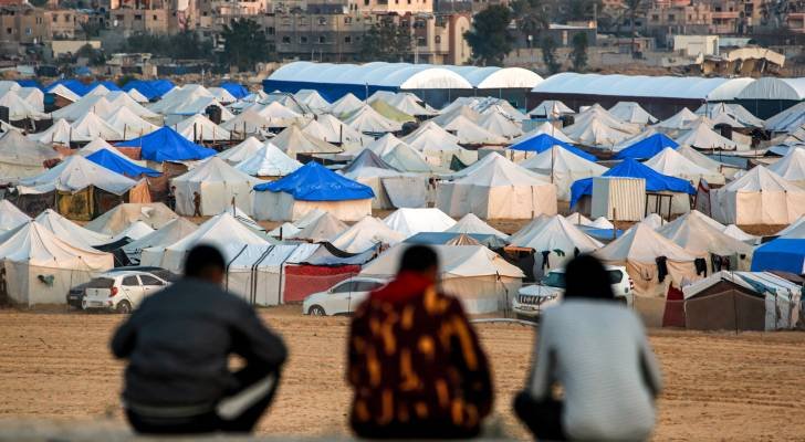 رجال يجلسون معًا ويطلون على منظر الخيام التي تؤوي الفلسطينيين الذين نزحوا شمال خان يونس
